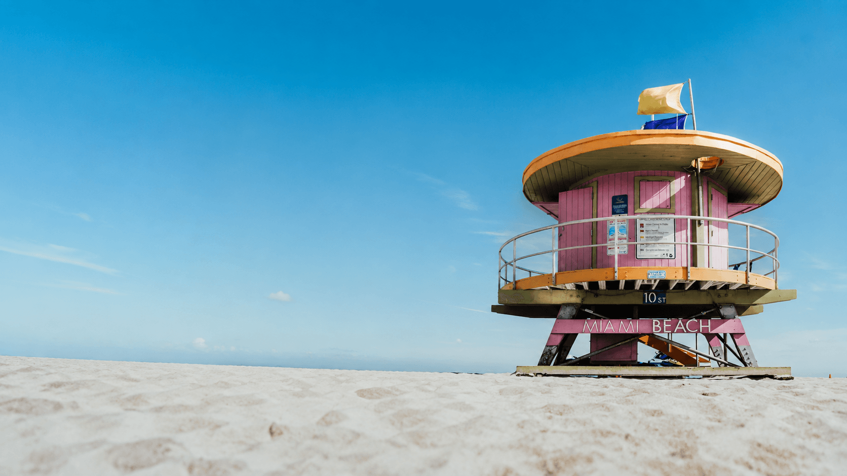 Pink and olive lifeguard tower on the sands of Miami Beach, under a bright blue sky.